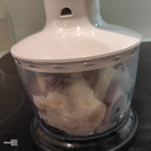 A food procesor with cod, onions, parsley, garlic and salt